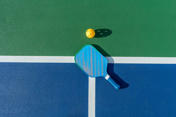 High-angle view of pickleball paddle and ball on court surface