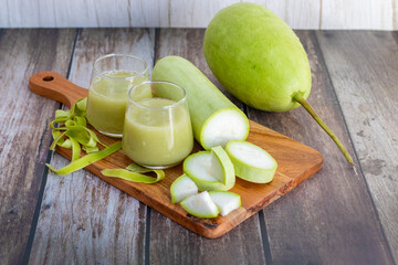 Two glasses of fresh bottle gourd juice, peeled slices, and whole gourd are placed on a wooden...