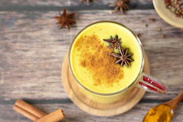 Golden milk (turmeric latte drink) with cinnamon and anise star on wooden table. Top view.