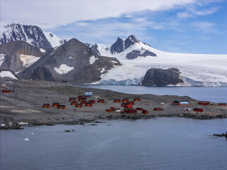 Aerial view of red-roofed buildings nestled on a rocky shore with snow-capped mountains rising in the background, Seymour Island, Antarctica.