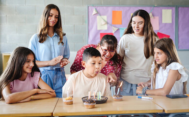 Birthday party at School. Children celebrating hispanic boy party singing and blowing cake candles...
