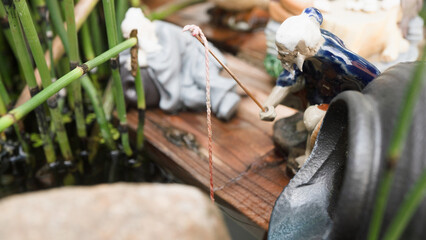 Serene miniature scene depicts figurine of elderly man fishing beside small pond, surrounded by...