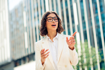 Confident young businesswoman in white professional attire gesturing in a modern urban setting...