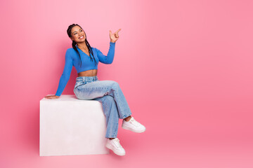 Young cheerful woman in casual attire sits against pink background exuding charm and confidence...