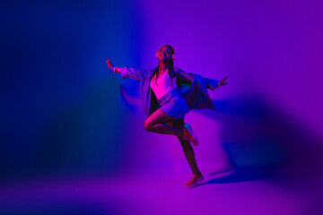 Young woman dancing in vibrant neon lights showcasing modern fashion and energy in a colorful atmospheric environment