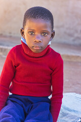 Africa village, african child sited on a blanked on the ground outdoors in the yard