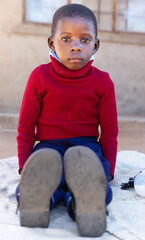 Africa village, african child sited on a blanked on the ground outdoors in the yard