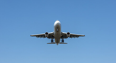 Obraz premium Large Passenger Airplane Flying Overhead Against Clear Blue Sky