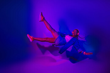 Young woman dancing with vibrant neon lighting in a casual outfit, showcasing joyful energy in a...