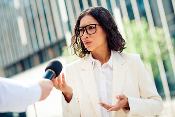 Confident businesswoman speaking outdoors in professional attire during an urban interview setting