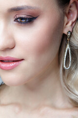 Beauty portrait of young blonde woman. Female Woman wearing earrings with rhinestones.
