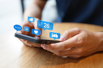 Close Up of Hands Holding a Smartphone with Social Media Notification Icons Floating Above Representing Digital Communication and Online Engagement on a Wooden Table