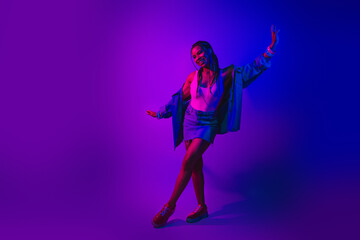 Youthful woman enjoying a vibrant neon dance party in vivid lighting colors wearing trendy denim...