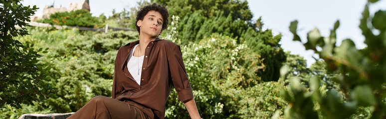 Young man enjoys summer day in a stylish outfit amidst lush greenery in the park