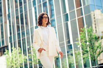Confident businesswoman walking in urban environment with modern architecture under sunny daylight...