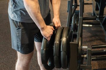Sporty young man and bodybuilder picking up heavy dumbbell at gym or fitness center. Close up