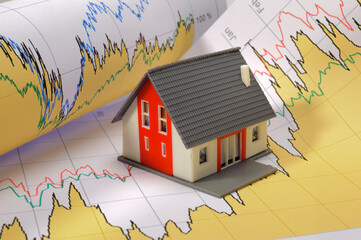 Ein Modellhaus steht symbolisch auf einem Chart für steigende Immobilienpreise