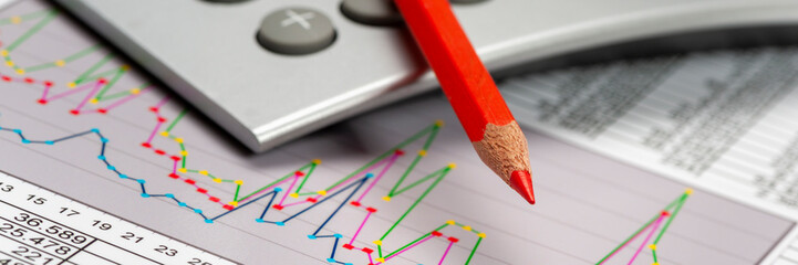 Ein Rotstift liegt auf einem Taschenechner und Chart als Symbol für Einsparungen in Finanzen und...
