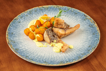 Crispy fried fish served with golden potato balls, creamy yellow sauce, microgreens, and a wedge of lemon on a rustic plate