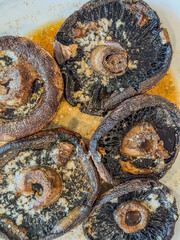 Grilled portobello mushroom caps topped with parmasean cheese, spices, and butter on a white plate