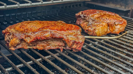 Two, thick, beef, ribeye steaks cooking on a grill with an inserted temperature probe