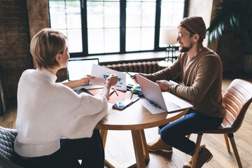 Two freelancers discuss a world map and digital statistics, using laptops and printed data,...
