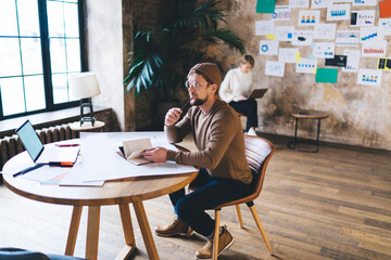 Freelancer reflects on idea execution holding notebook, surrounded by laptop, digital charts and...