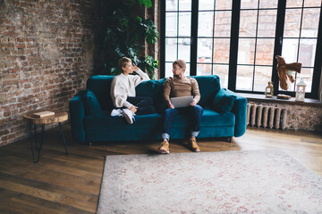 Two coworkers sit relaxed, discussing app layout ideas while casually positioned with a laptop,...
