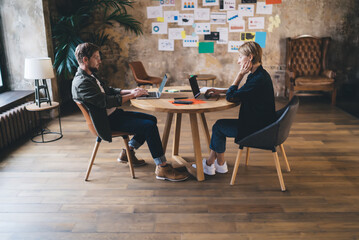 Man and woman working remotely across table with laptops, representing flexible co-working,...