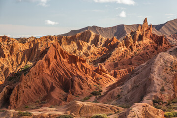 Stunning landscape of Charyn Canyon, Kazakhstan.  Red sandstone formations create a dramatic, textured scene under a partly cloudy sky.  Perfect for travel, nature, and geological content.