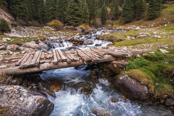 Rustic wooden bridge over a cascading mountain stream in the Tian Shan mountains of Kyrgyzstan.  A...