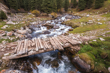 Rustic wooden bridge over a cascading mountain stream in the Tian Shan mountains of Kyrgyzstan.  A...