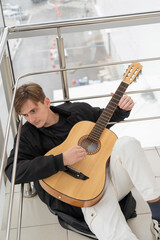 Caucasian man sitting on a staircase and playing guitar. 