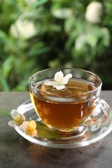 Aromatic jasmine tea in glass cup and flowers on grey table outdoors, closeup
