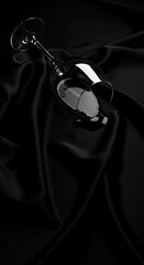 A dark, elegant wine glass lies overturned on a luxurious, draped black satin fabric, creating a moody and sophisticated image.
