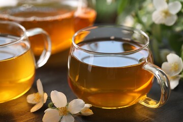 Tasty jasmine tea in cups, teapot and flowers on black table, closeup