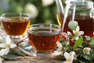 Tasty jasmine tea in cups, teapot and flowers on wooden table, closeup