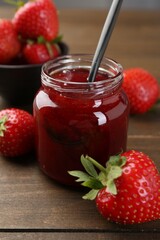 Tasty homemade strawberry jam in glass jar and berries on wooden table, closeup