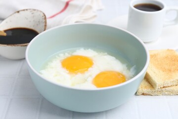 Traditional asian breakfast with half-boiled eggs in bowl, soy sauce, bread and coffee on white...
