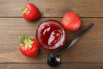 Tasty homemade strawberry jam in glass jar and berries on wooden table, flat lay