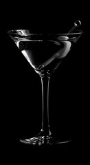 A classic martini in a stemmed glass with an olive on a pick is sharply contrasted against a deep black background, highlighting the drink's clarity.