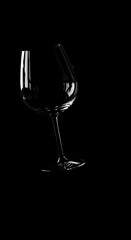 A solitary, empty wine glass is dramatically silhouetted against a stark black background, emphasizing its elegant shape and delicate stem.