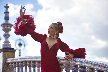 Young, beautiful, blonde woman in red flamenco dress, flowers in her hair and gold jewelry,...