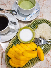 Traditional Thai dessert mango sticky rice served on a ceramic plate with coconut milk. Accompanied...