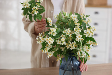 Woman making bouquet of jasmine branches at wooden table, closeup