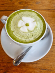 A cup of matcha latte in a white cup with a saucer and a spoon, featuring delicate latte art in the...