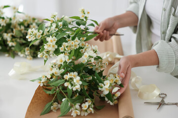 Woman making bouquet of jasmine branches at white table, closeup