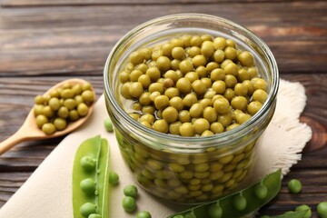 Pickled peas in jar and pods on wooden table, closeup