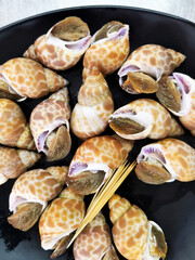 Steamed spotted babylon snails served on a black plate with wooden skewers