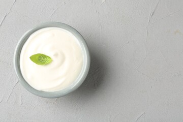 Tasty yoghurt with basil in bowl on light grey table, top view. Space for text
